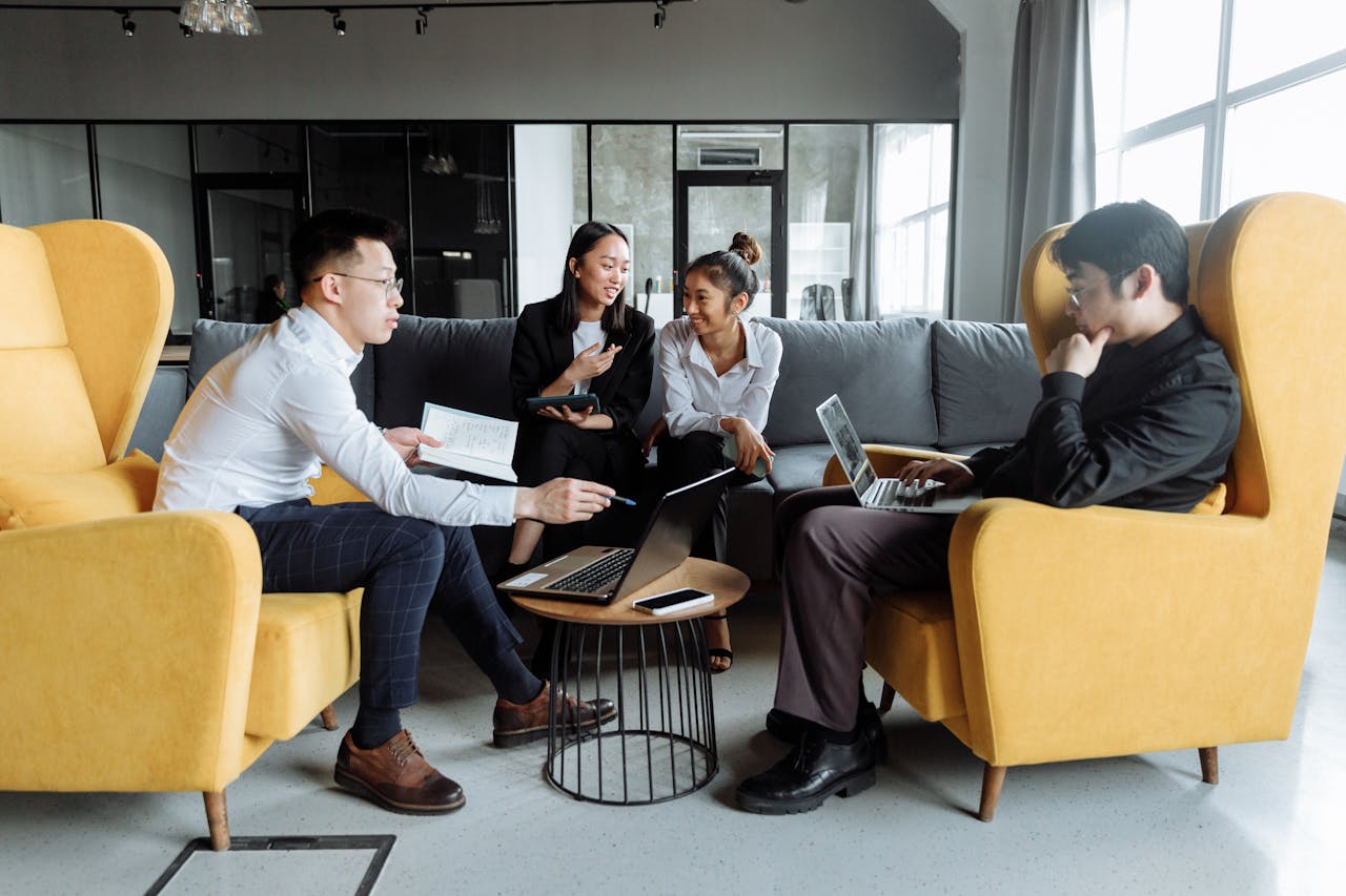 Four young professionals collaborating in an office setting with laptops and notes.